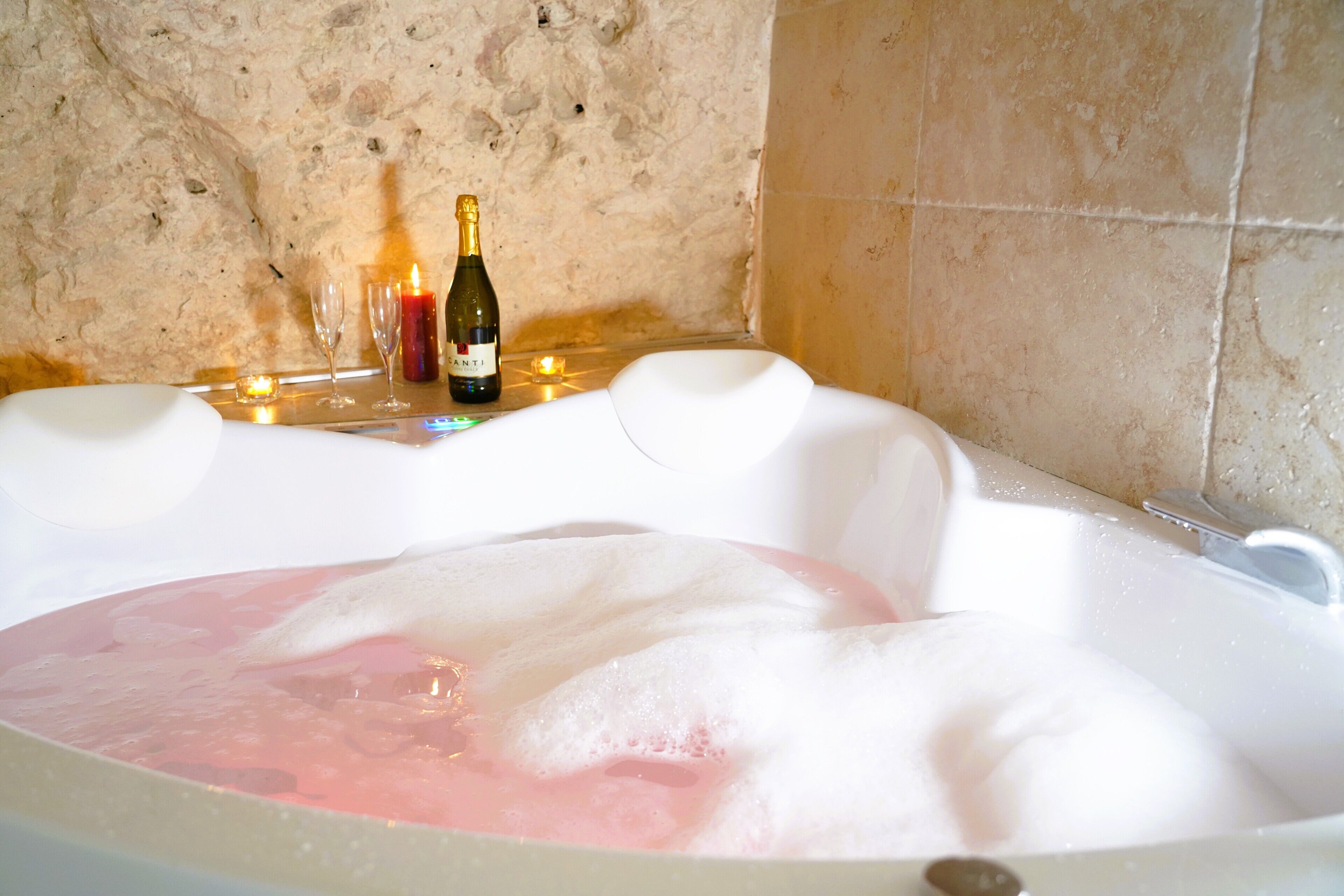 Una vasca da bagno piena di bolle, una bottiglia di champagne e due bicchieri su un tavolo.