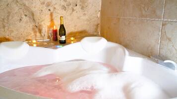 Una vasca da bagno piena di bolle, una bottiglia di champagne e due bicchieri su un tavolo.