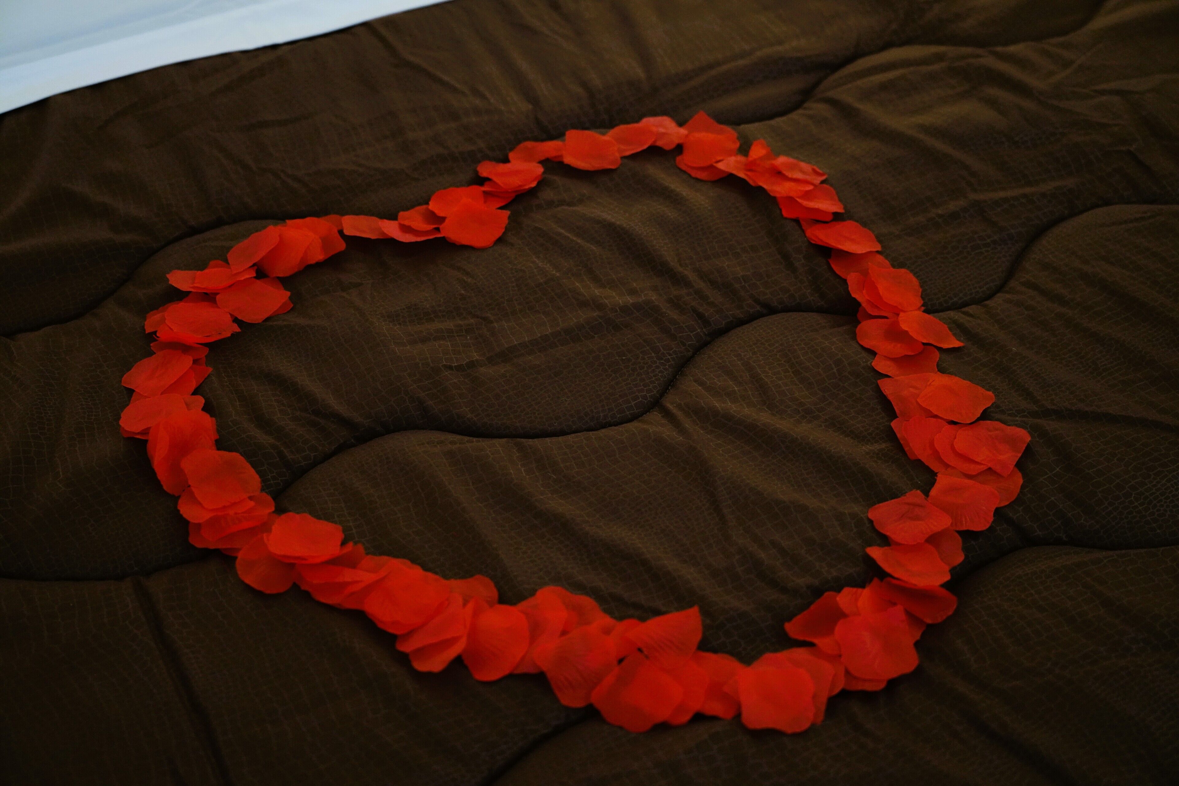 Een hartvormige decoratie van rode bloemen op een bruine stoffen ondergrond.