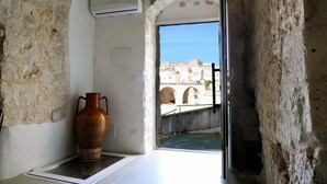Une pièce rustique avec un mur en pierre, une fenêtre donnant sur des bâtiments et un vase posé sur une étagère.