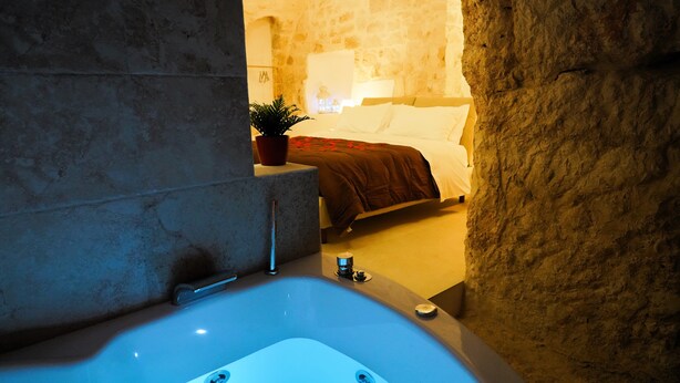 Une salle de bain aux murs de pierre, avec une baignoire, une plante en pot et un lit en arrière-plan.