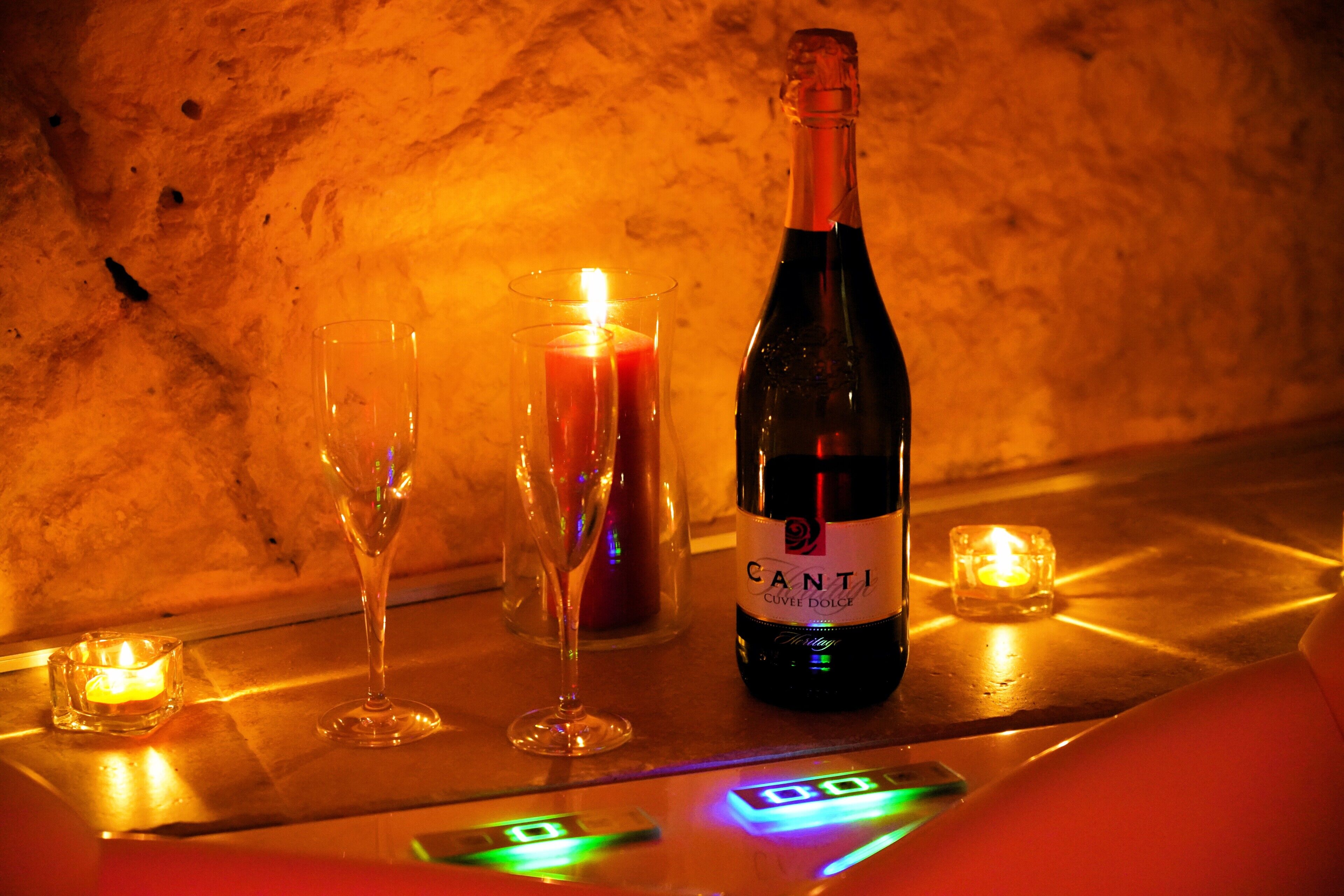 A bottle of Canti wine, two glasses, and a lit candle on a table with a marble background.