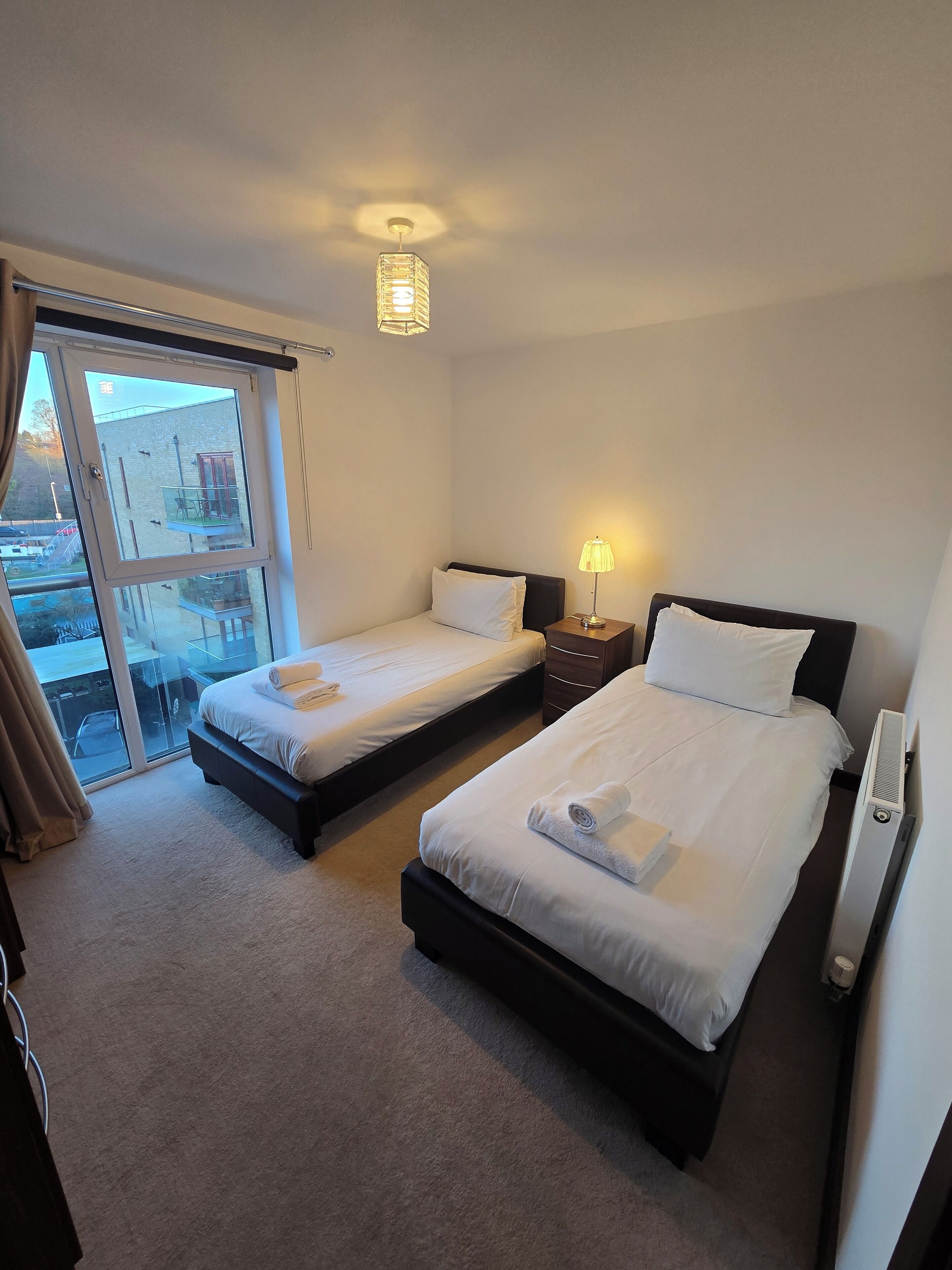 A hotel room with two single beds, a large window with a view of the outside, and a ceiling light fixture.