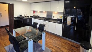 A modern kitchen with white cabinets, black appliances, and a glass dining table with chairs. - Tranquil 2 Bed, 2 Bath Apartments walking distance from the Uxbridge town centre (Denham)