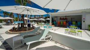 Un área junto a la piscina con sillones de descanso, sombrillas y un restaurante.