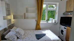 A bedroom with a bed, a washing machine, and a window with curtains. - Cosy, Quiet, Studio Flat (Isleworth)