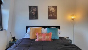 Ein ordentlich bezogenes Bett mit schwarzer Bettdecke, mehreren Kissen und zwei an der Wand befestigten Kunstwerken.