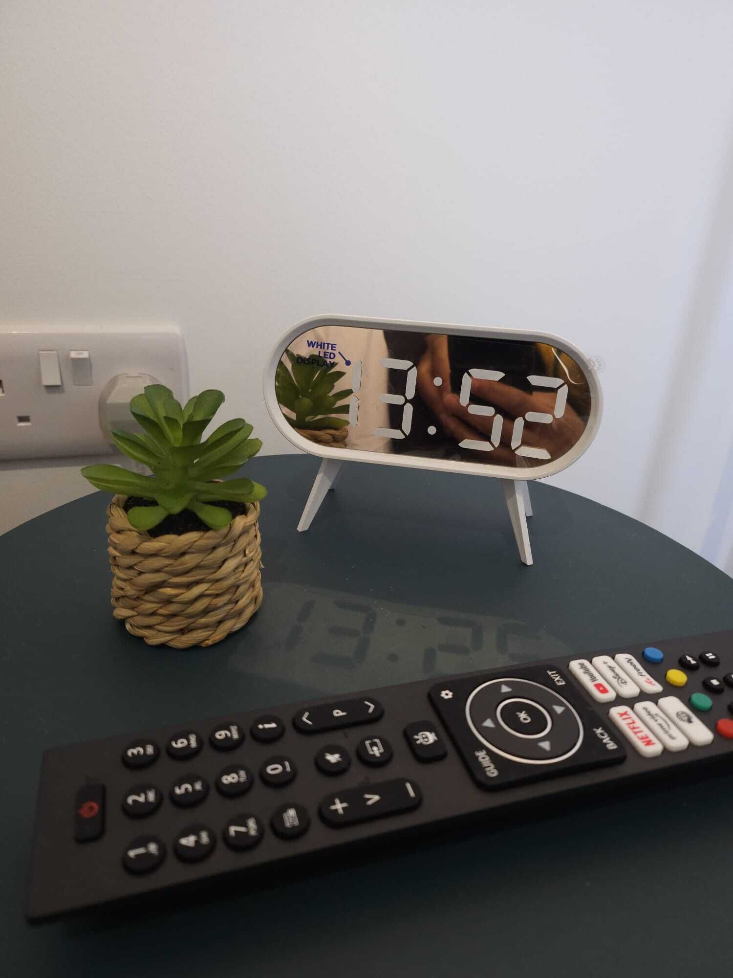 A remote control, a small potted plant, and a digital clock on a table.