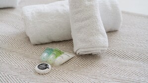 A neatly folded white towel, two small tubes of cream, and a round container on a textured beige surface.