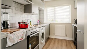A modern kitchen with a built-in oven, a washing machine, and a window with blinds.