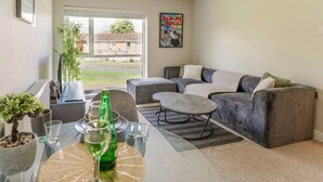 A modern living room with a grey sofa, a glass coffee table, and a view of a residential area.