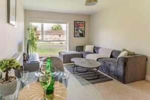 A modern living room with a grey sofa, a glass coffee table, and a view of a residential area. - Solihull House | Free Parking | NEC | Airport (Solihull)