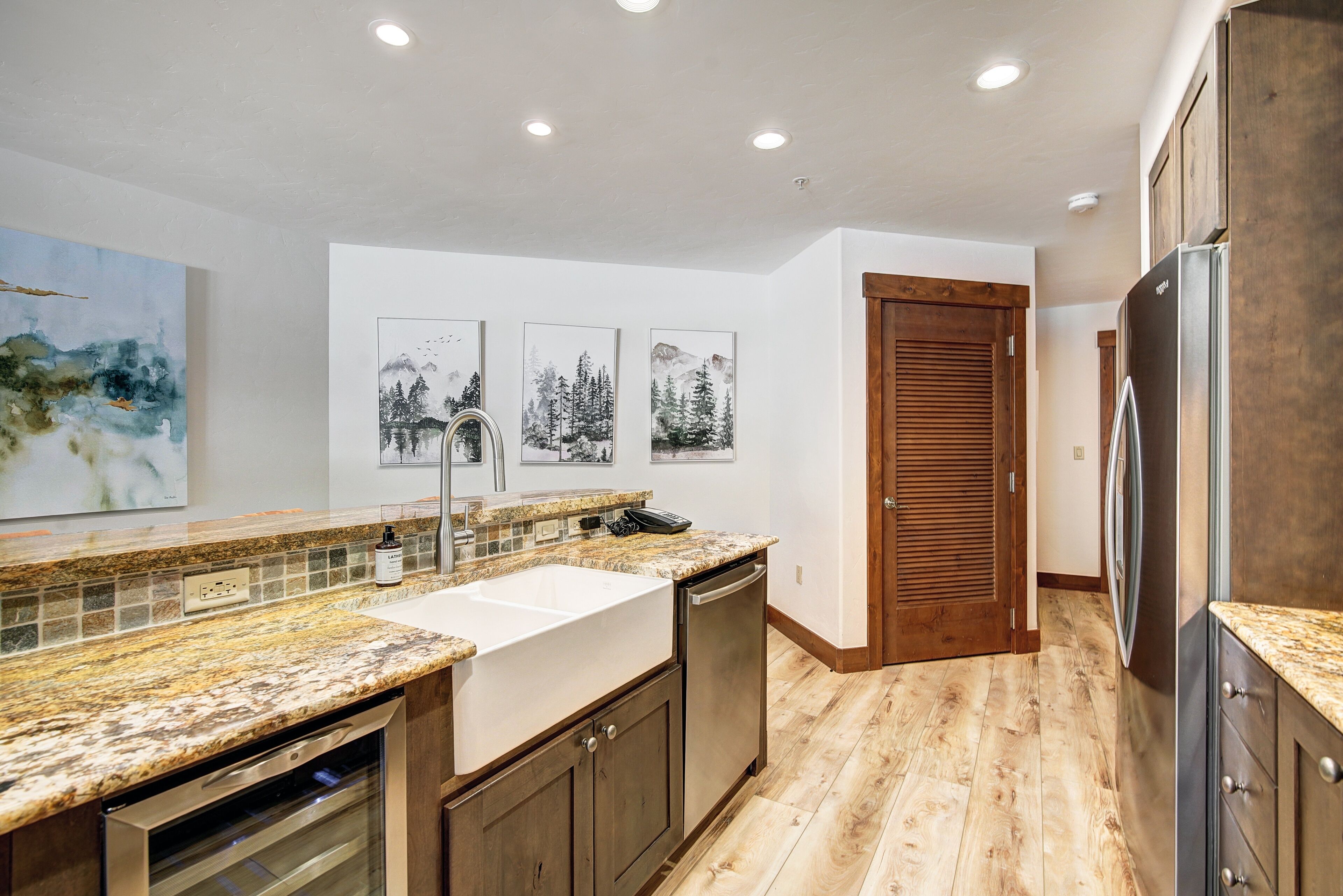 Una cocina moderna con encimeras de granito, lavavajillas integrado, armarios de madera y piso de madera.