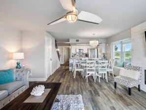 A spacious living area with a dining table, white chairs, a sofa, and a ceiling fan. - Pier Perfection K101 3 Bedroom Condo (Rockport)