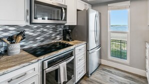 A modern kitchen with white cabinets, a stainless steel refrigerator, a microwave, and a stove. - Pier Perfection K101 3 Bedroom Condo (Rockport)