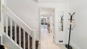 A hallway with a staircase, a coat rack, and a door leading to a dining area.