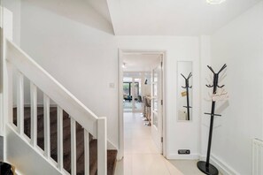 Un couloir avec un escalier, un porte-manteau et une porte donnant sur une salle à manger.