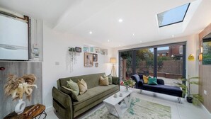 A modern living room with a sofa, a coffee table, and a dining table. There is a large window with a view of the outside.