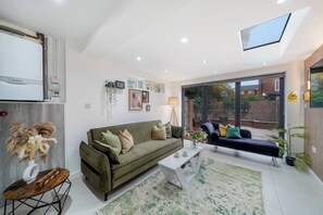 Un salon moderne avec un canapé, une table basse et une table à manger. Une grande fenêtre offre une vue sur l’extérieur.