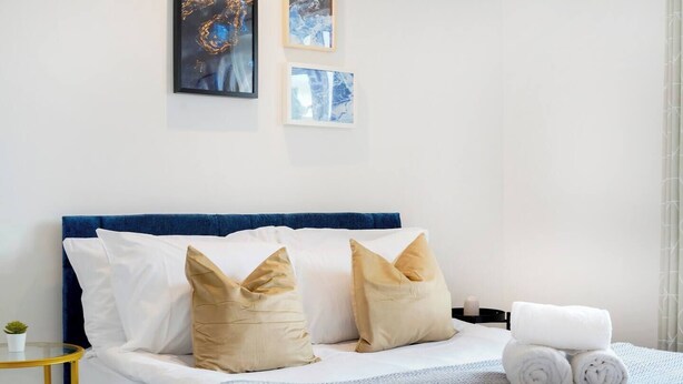 A hotel room with a bed, pillows, a bedside table with a lamp, and artwork on the wall.