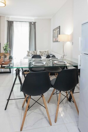 A modern dining area with a glass table, black chairs, and a white refrigerator. - Olia Urban Luxury Studio (Zografou)