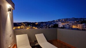 A rooftop terrace with two white lounge chairs and a table, overlooking a cityscape at dusk. - Private Boutique Hotel in Arcos de la Frontera – Exclusive Use - 4 Suites (Arcos de la Frontera)