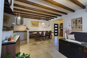 A spacious living area with a dining table, chairs, and a sofa. There is a kitchen area with cabinets and a countertop. The room has wooden beams on the ceiling and a wall-mounted decoration. - Villa Peaceful Valley With Heated Pool (Sestanovac)