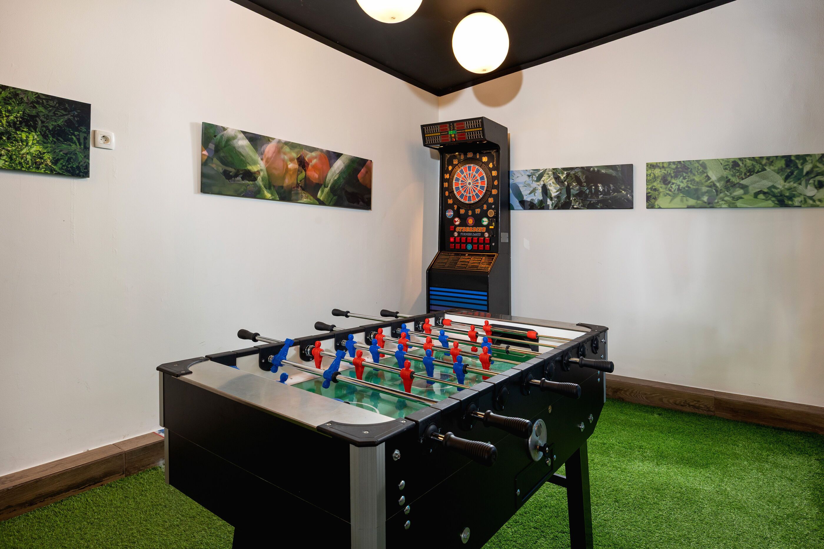 A foosball table in a room with green artificial turf, surrounded by four framed botanical paintings on the walls.
