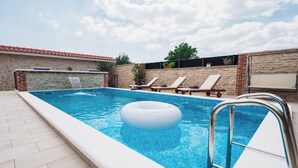 Une piscine rectangulaire dotée d’une cascade intégrée, entourée de murs en pierre et d’une terrasse carrelée.