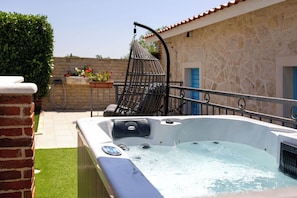 Un bain à remous doté de fonctions de spa, un fauteuil suspendu et un bâtiment en pierre avec des portes bleues en arrière-plan.