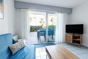 Una sala de estar con sofá, televisor, mesa de madera y puerta corrediza de vidrio que da a un patio exterior.