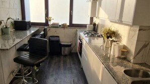 A modern kitchen with dark wood flooring, white cabinetry, a bar stool, and a window providing natural light. - Enjoyable 4-bed, 2.5 bath apartment in the heart of London - Hoxton Zone 1 (London)