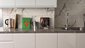 A modern kitchen with white cabinets, a granite countertop, a kettle, a coffee maker, and two cookbooks. - Enjoyable 4-bed, 2.5 bath apartment in the heart of London - Hoxton Zone 1 (London)