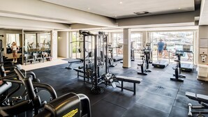 Ett gym med olika typer av träningsutrustning, stora fönster och utsikt över omgivningen.
