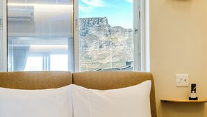 Ett hotellrum med en säng, ett fönster med utsikt över ett berg och ett nattduksbord med en telefon.