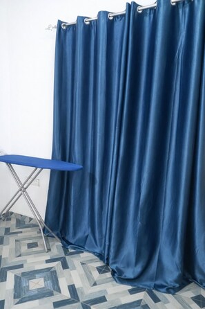 Ein Zimmer mit blauer Vorhang, einem Klappbügelbrett und einem gemusterten Boden.