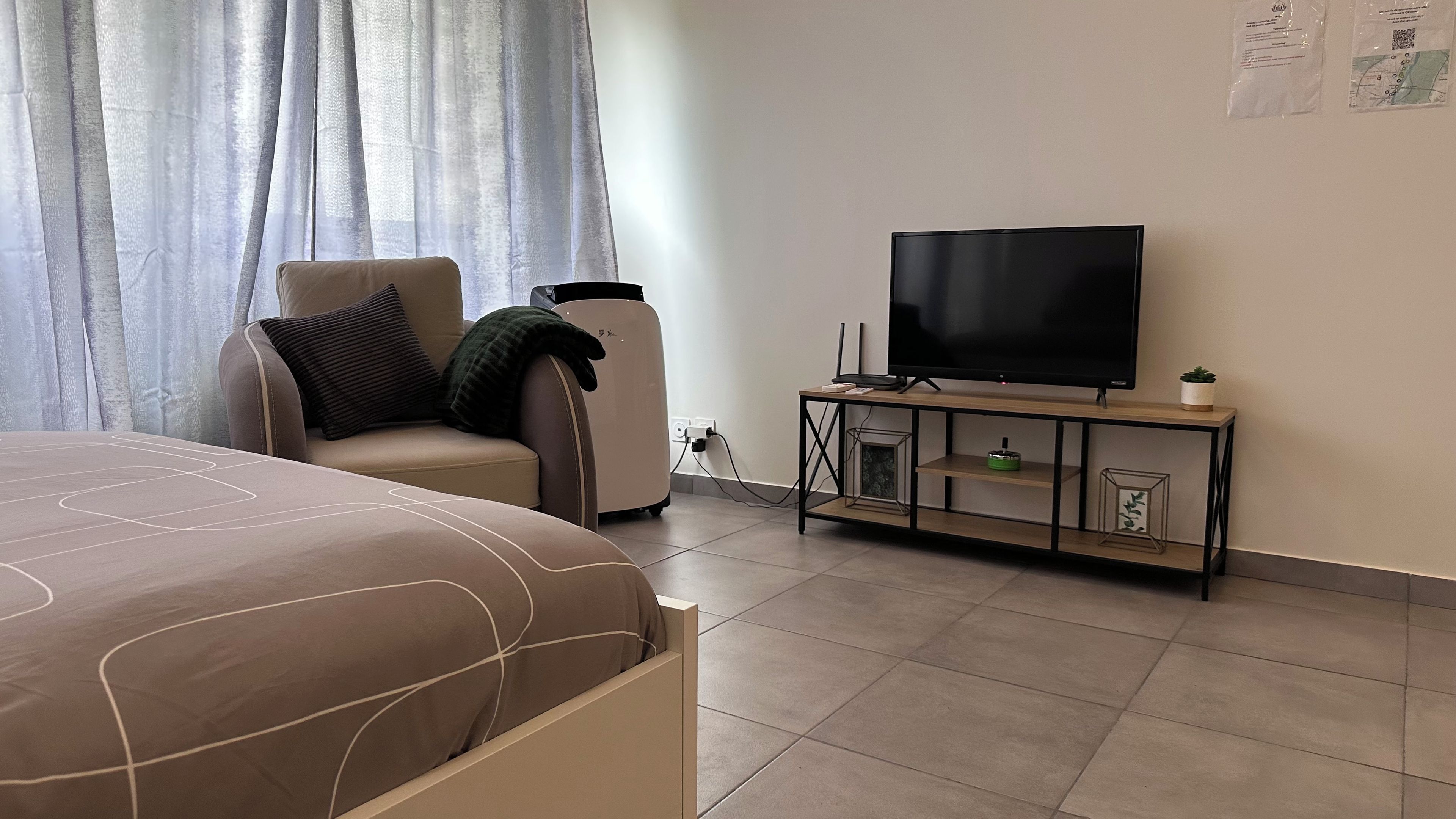 A hotel room with a bed, a chair, a TV on a stand, and a small table with a plant.