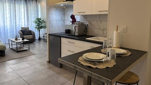 A modern kitchen with a built-in oven, a dining area with a table set for two, and a living area with a sofa and a coffee table. - Whole apartment - Studio Noéa (Mâcon)