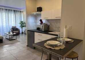 A modern kitchen with a built-in oven, a dining area with a table set for two, and a living area with a sofa and a coffee table. - Whole apartment - Studio Noéa (Mâcon)
