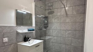A modern bathroom with a glass shower enclosure, a white sink, and a mirror above it. - Whole apartment - Studio Noéa (Mâcon)