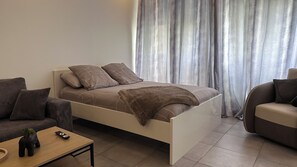 A modern bedroom with a bed, a sofa, a coffee table, and a small plant. - Whole apartment - Studio Noéa (Mâcon)