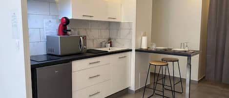 Una cocina moderna equipada con lavavajillas, cafetera, fregadero y un taburete de bar.