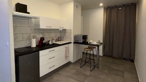 A compact kitchen with white cabinets, a black countertop, and a small stool. - Whole apartment - Studio Noéa (Mâcon)