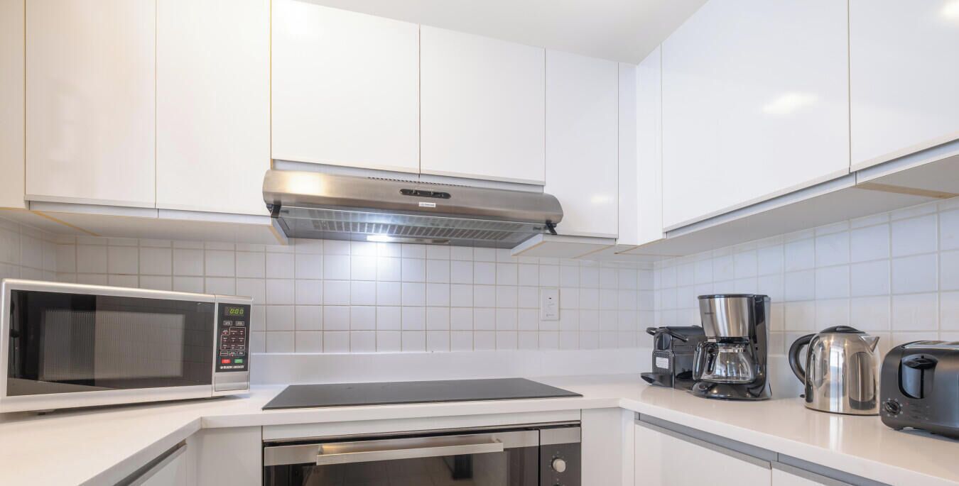 A modern kitchen with white cabinets, a built-in microwave, a coffee maker, a kettle, and a toaster.