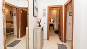 A hallway with wooden doors, a light-colored tiled floor, a small wooden cabinet, and a framed picture on the wall. - Red City Elegant Stay (MARRAKECH)