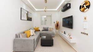 A modern living room with a grey sectional sofa, a black coffee table, and a mounted flat-screen TV. - Red City Elegant Stay (MARRAKECH)