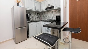 A modern kitchen with white cabinets, a stainless steel refrigerator, a black countertop, and a bar stool. - Red City Elegant Stay (MARRAKECH)