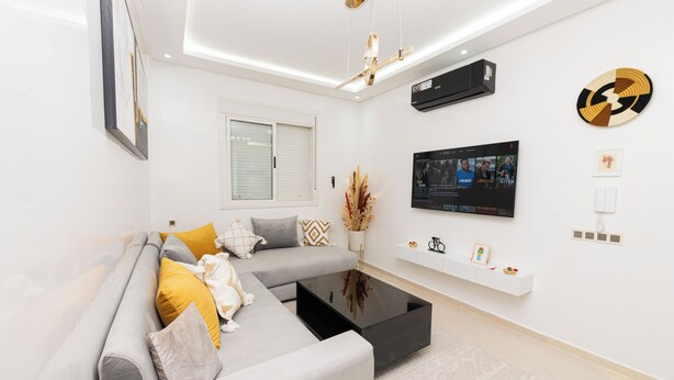 A modern living room with a grey sofa, black coffee table, and a mounted TV. - Red City Elegant Stay (MARRAKECH)
