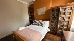 A bedroom with a wooden bed, a wooden wardrobe, and a shelf unit. - Where English Charm Meets Moroccan Soul - 1 Minute from Kensal Green Station (London)
