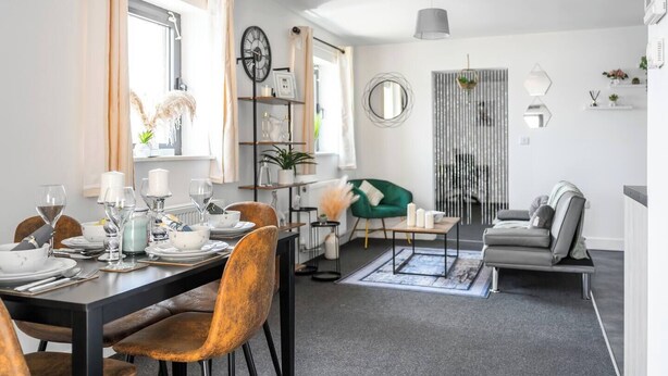 A modern dining area with a table set for four, a green armchair, and a grey sofa in a bright living space with a large window. - Modern 1-Bed Apartment with Parking near Heathrow (Slough)